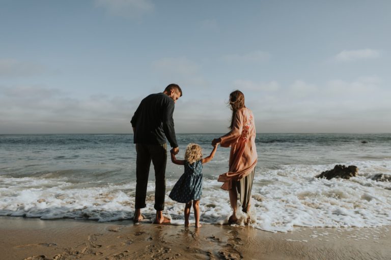 Image of a fmaily holding hands on the beach with waves coming in