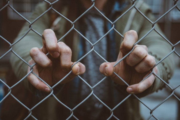 Image of hands holding on to a chain link fence