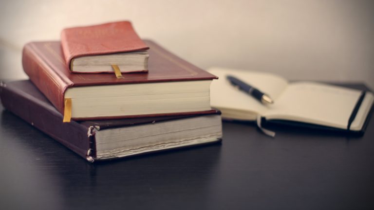 Image of leather bound books sitting on a table with an ink pen