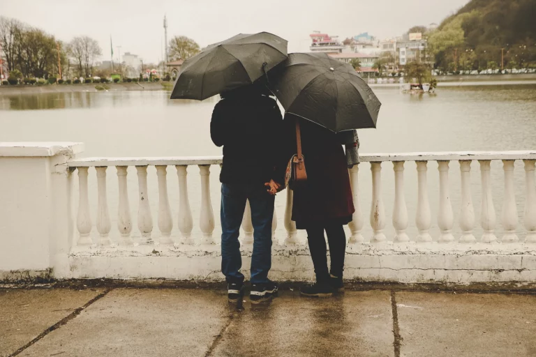 Image of spouses holding hands on a bridge under umbrellas. Green card for spouse.