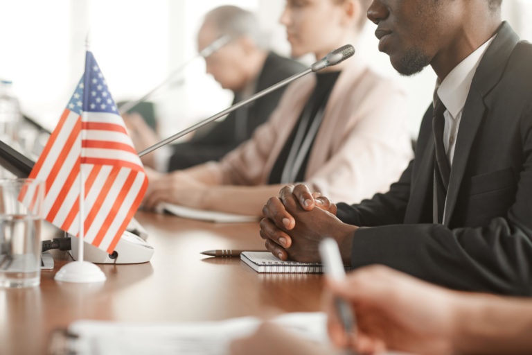 Image to represent US Board of Immigration appeals process. Man sitting behind desk at microphone with American flag.